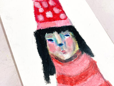Oil pastel drawing of a girl wearing pink polka dot winter hat.