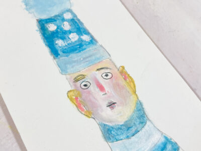 Oil pastel drawing of a boy wearing a blue polka dot winter hat.